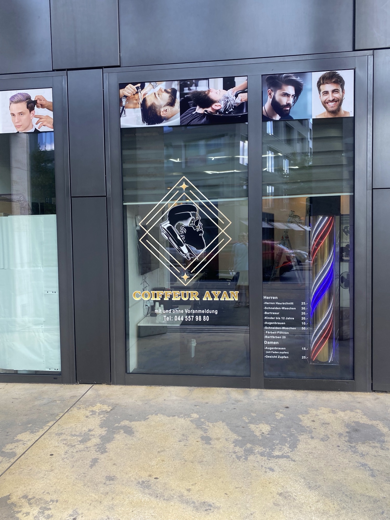 Eingang von Coiffeur Ayan mit goldenem Logo, Barberstange und Preisliste an der Glastür